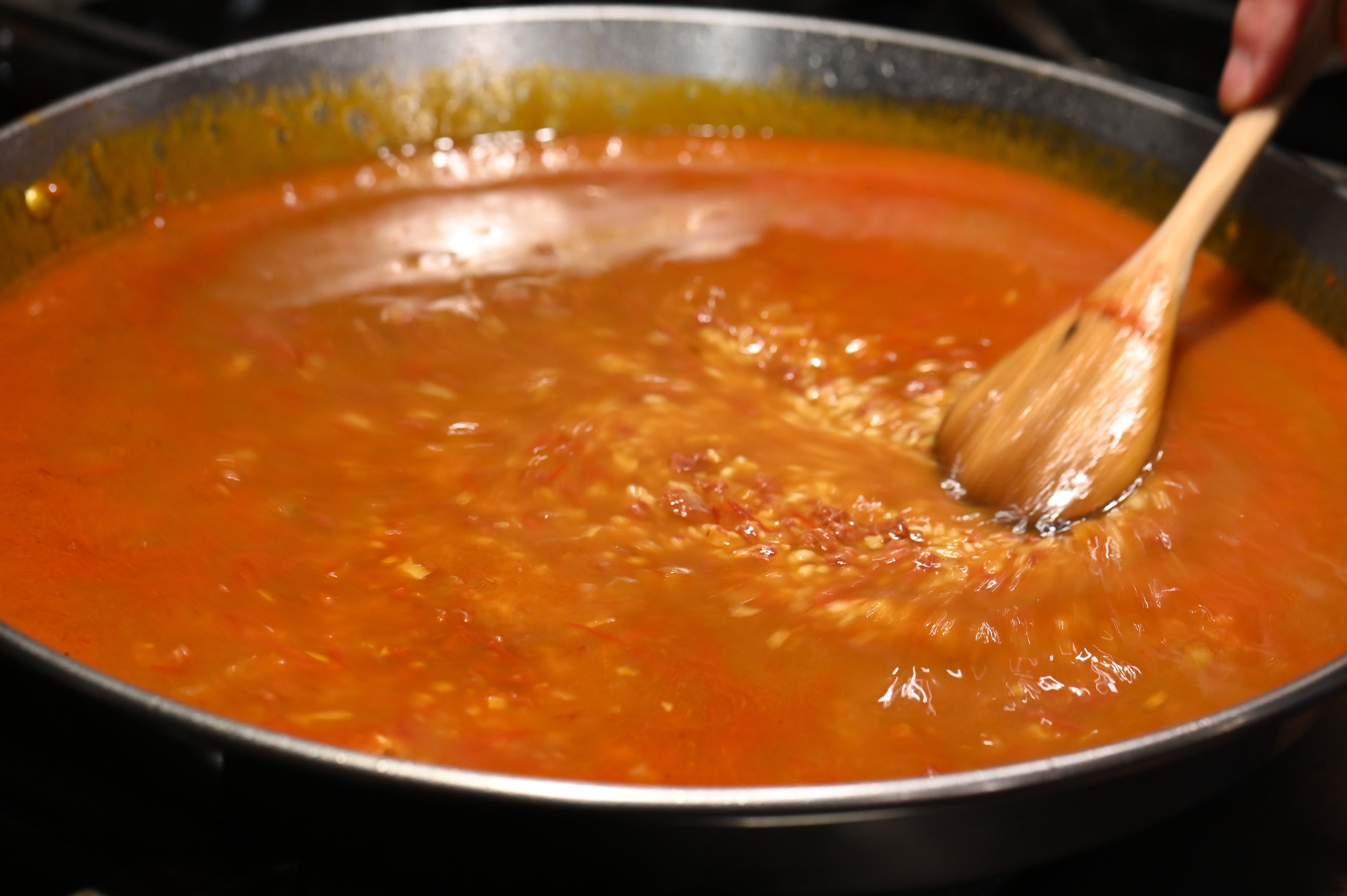 stirring stock into the paella with wooden spoon