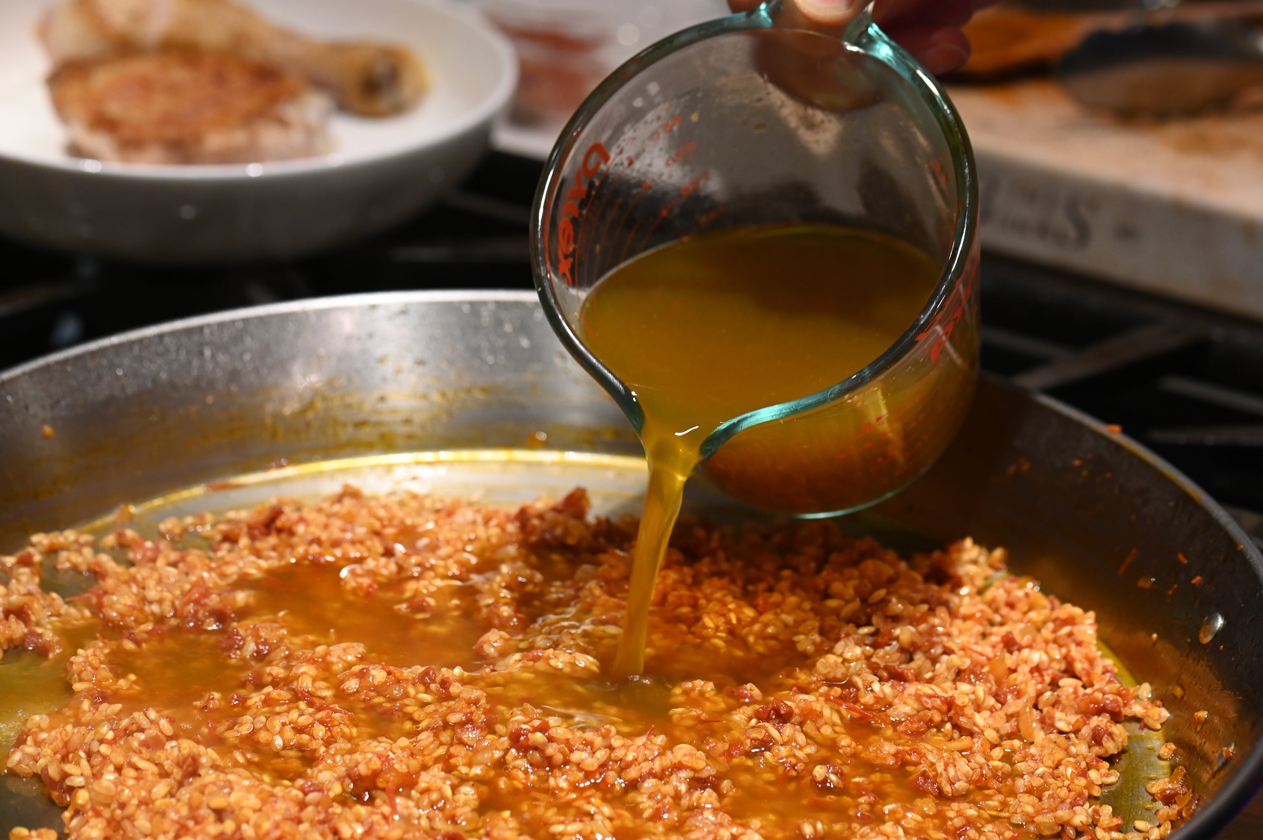 adding lobster and chicken stock to the paella pan