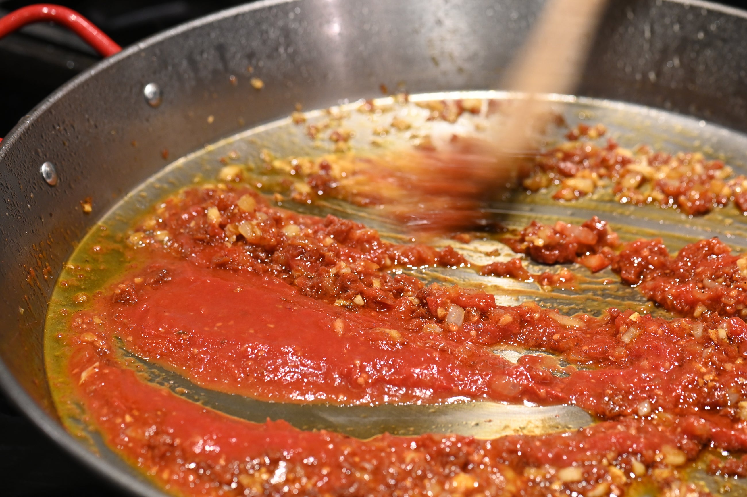 paella base with tomato being mixed with a wooden spoon