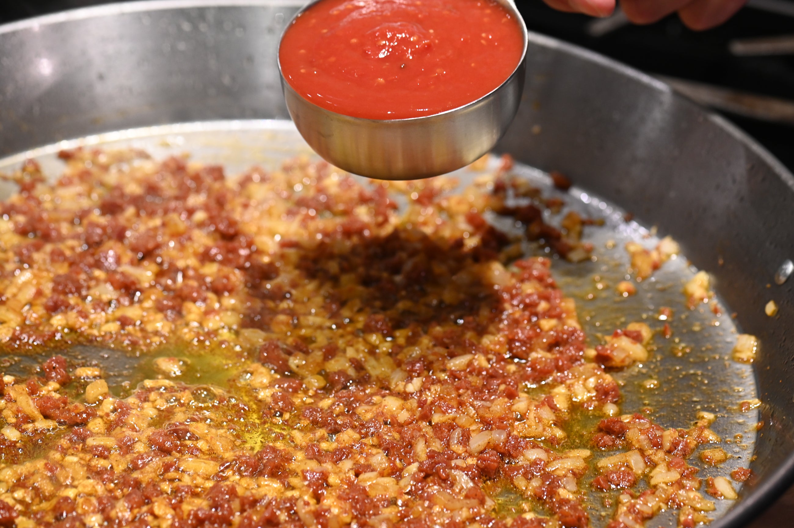 adding a cup of tomato to paella pan