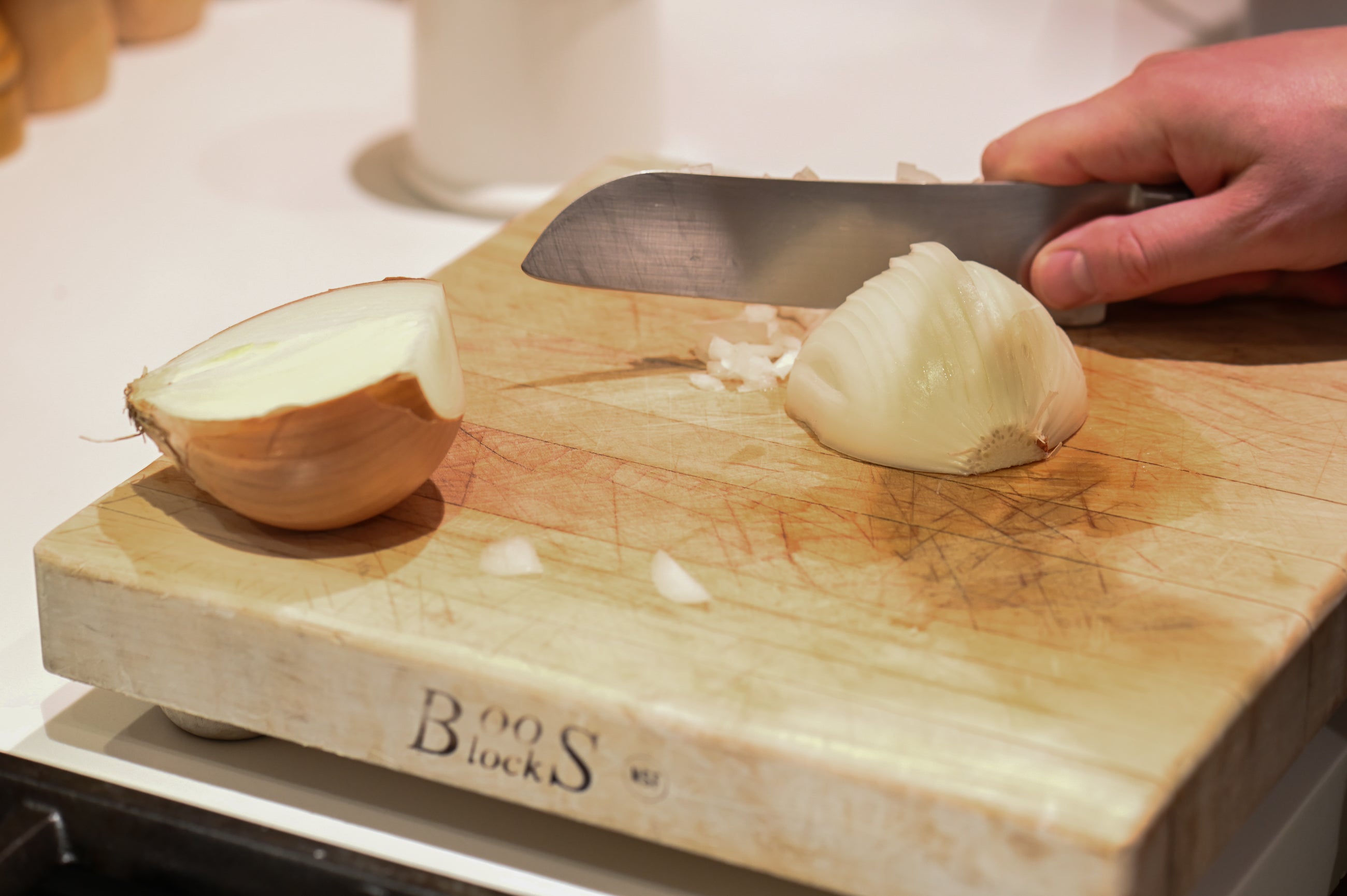 hands and knife dicing onion on a cutting board