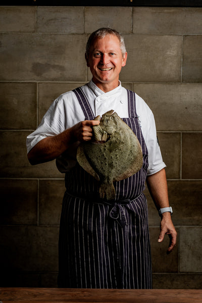Chef smiling holding Turbot against stone wall