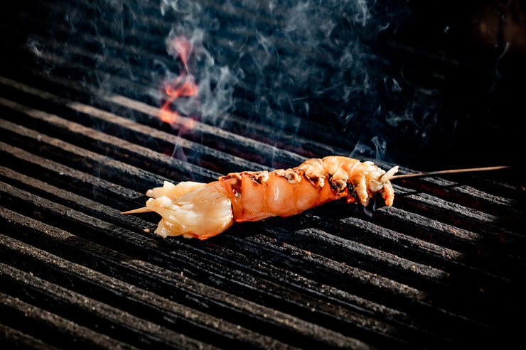 Spiny lobster tail skewer on grill with fire smoking