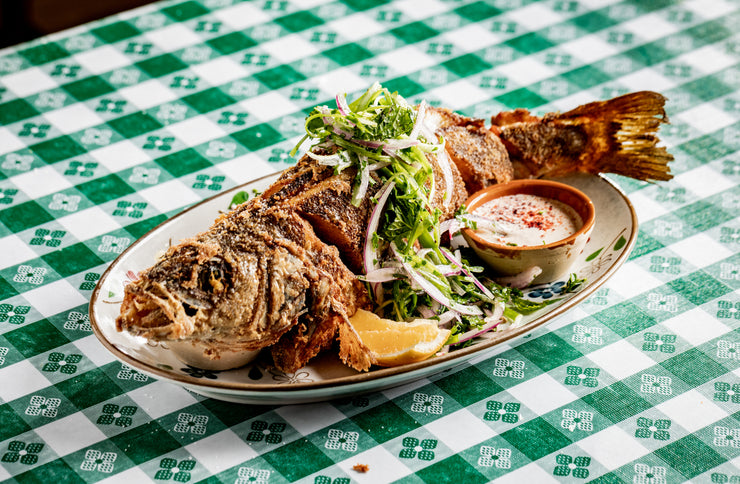 Whole Fried Branzino with salad on green picnic table