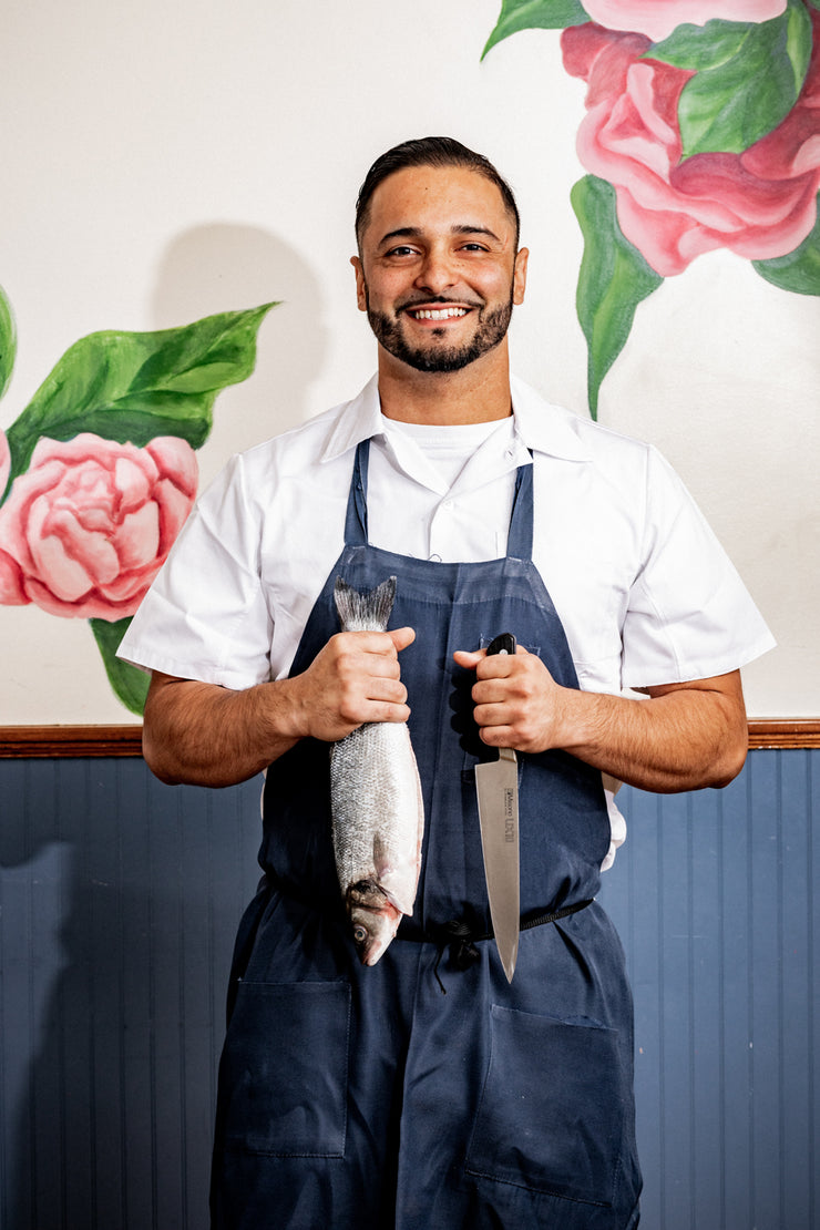 Chef smiling with knife and fresh Branzino in front of flower wallpaper