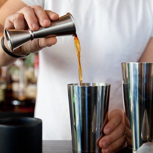 Person making cocktail pouring from jigger into cocktail shaker