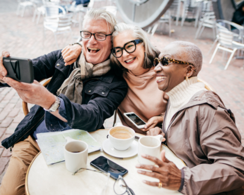 A man and two women taking a selfie together while sitting around a patio table enjoying coffee.