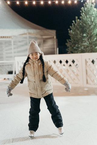 Girl wearing a winter coat and snow pants ice skating on a rink