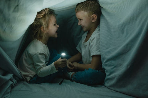 Little boy and girl laughing together in a cozy fort.