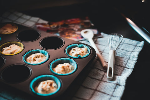 Cupcake batter in a cupcake tin with baking utensils beside it