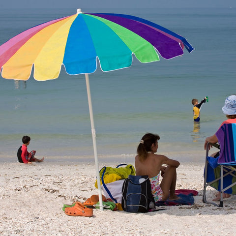 Family at beach using an umbrella for shade. The Twizzle Designs Earth Friendly Blog explores sunscreen.