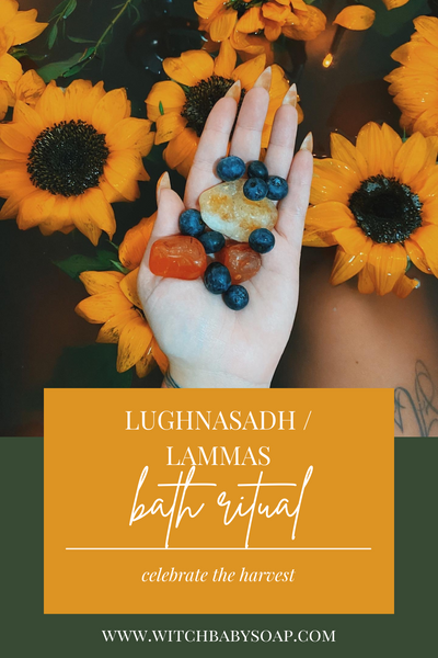 text: lughnasadh / lammas bath ritual next line reads: celebrate the harvest www.witchbabysoap.com photo of a hand outstretched with citrine, carnelian, and blueberries held over a bath with sunflowers floating in it