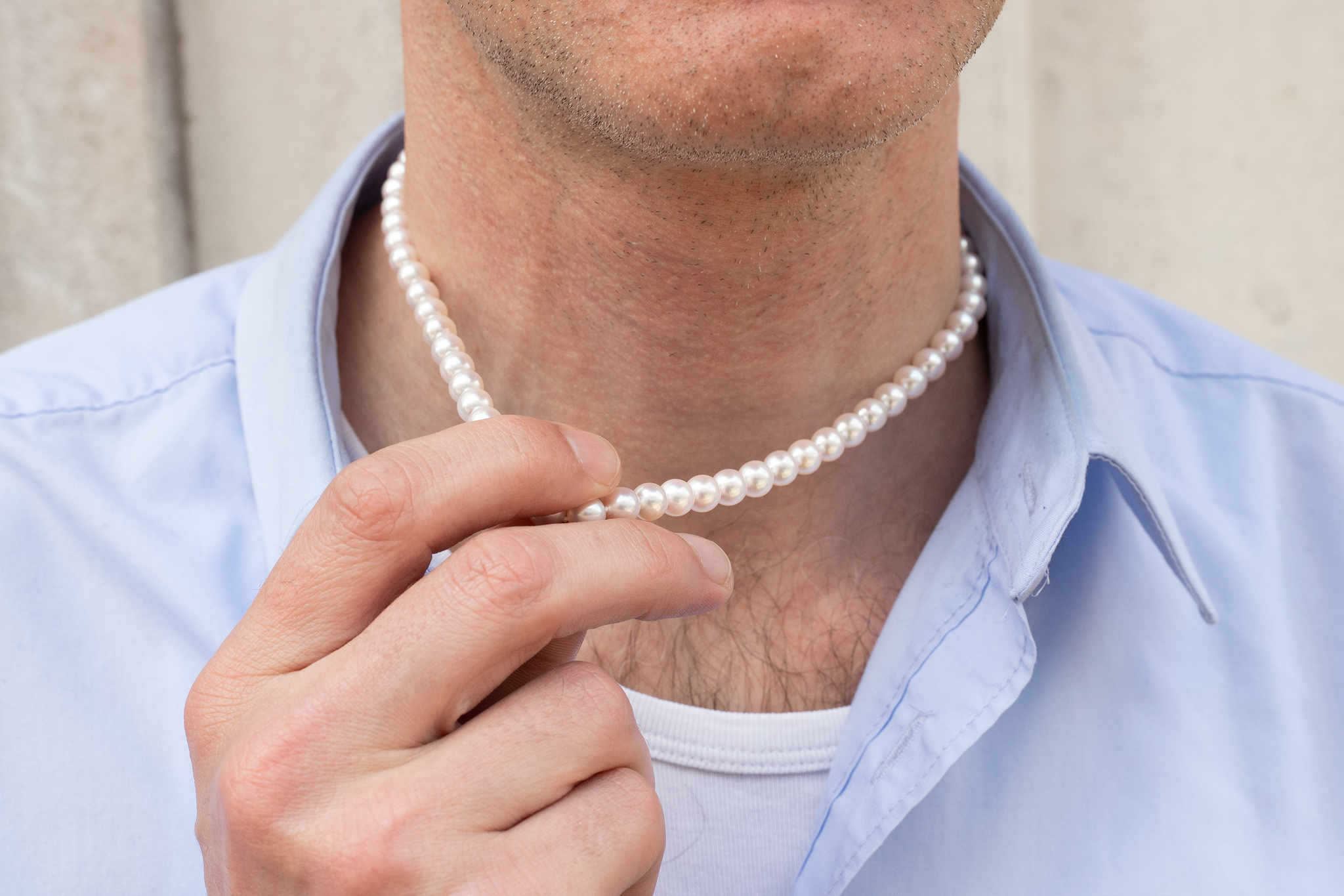 Man holding pearl necklace which sits on his neck