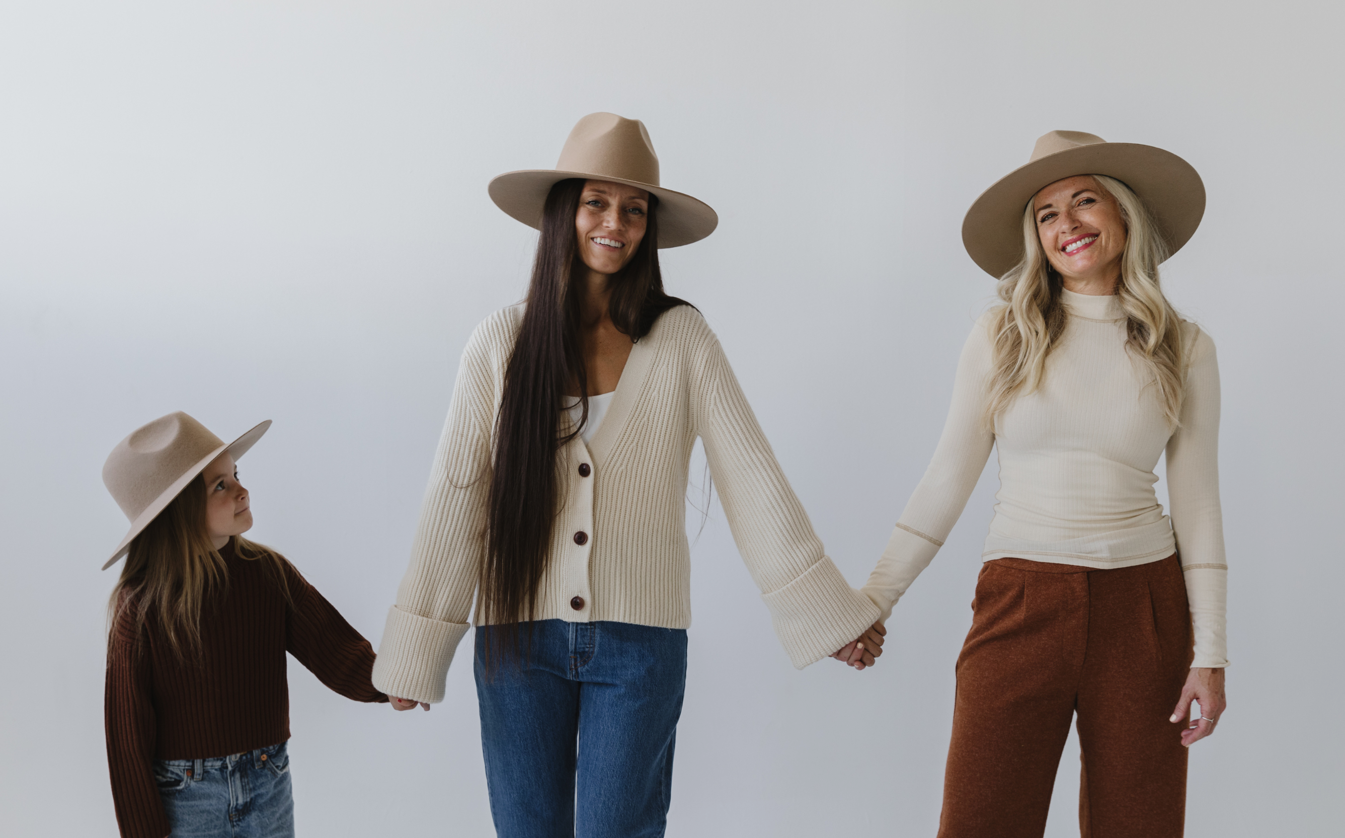 Two women and a child pictured in felt hats on a neutral background