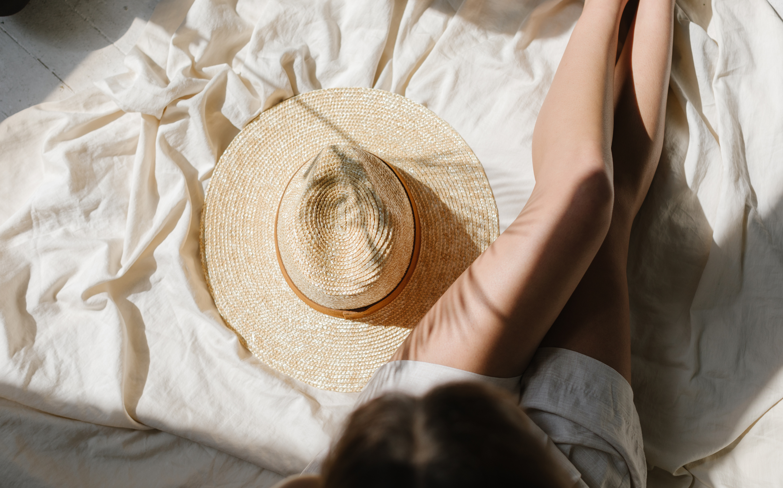 A natural, straw hat sits on a sheet next to a woman