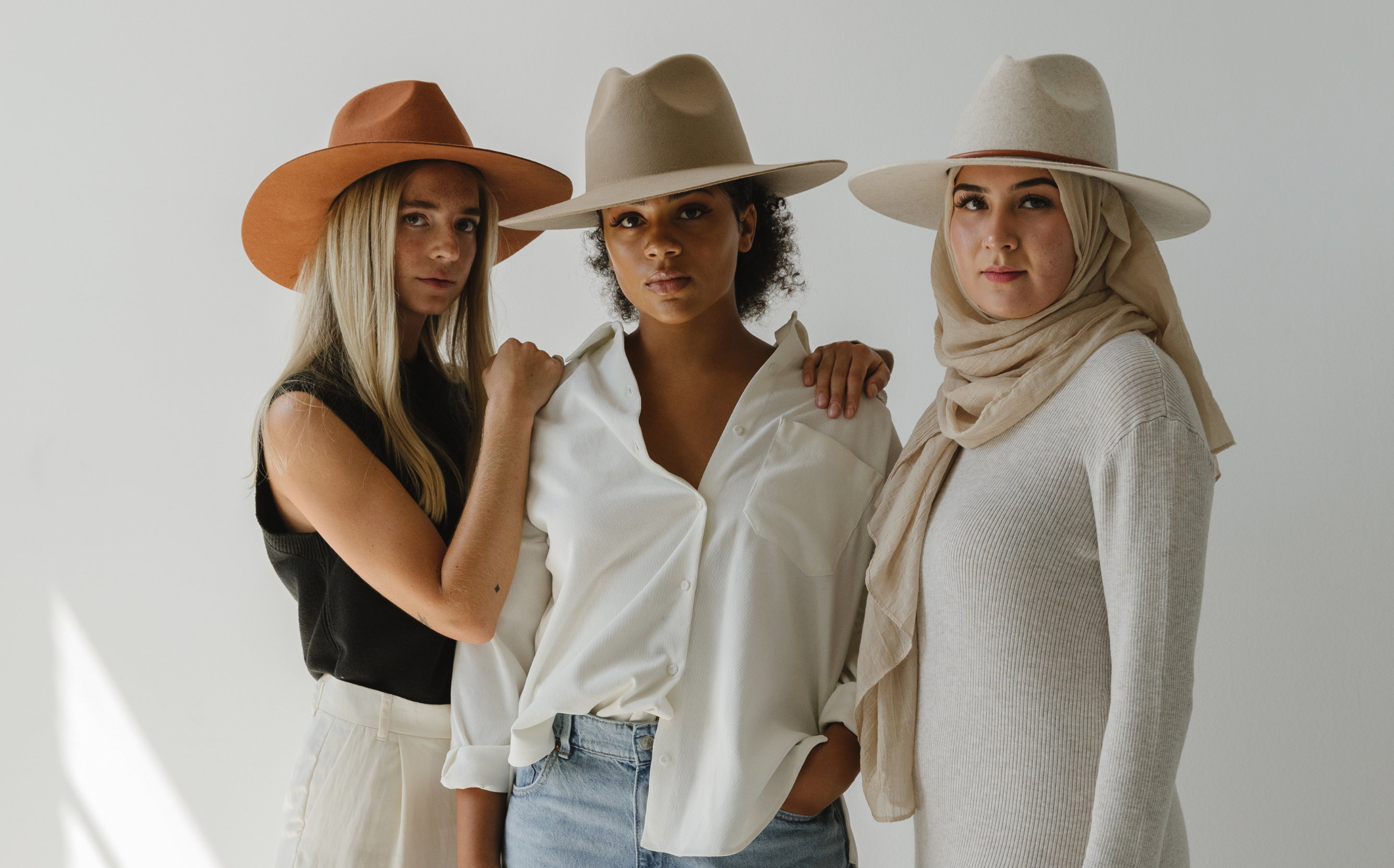 three women of different skin tones model a different hat color of the same wide brim fedora hat