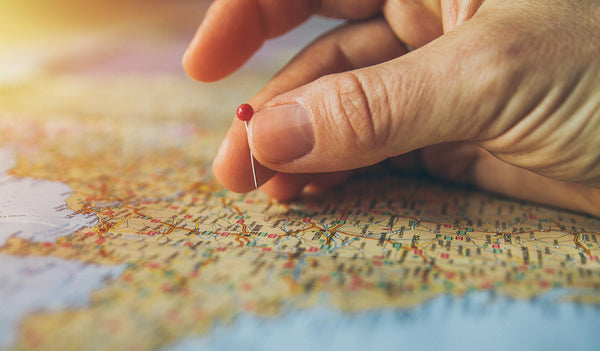 Hand placing pin on a large map to mark a location.