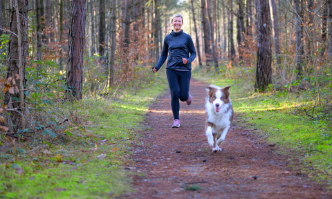 Owner and dog running in the forest exercising 