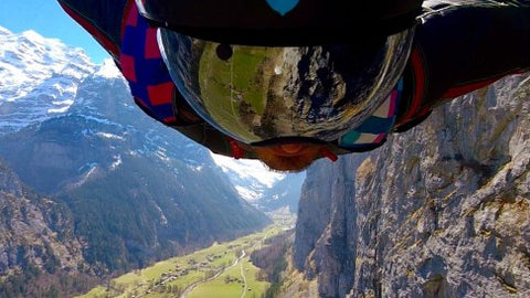 Wingsuit BASE jumping next to cliff above Lauterbrunnen Switzerland with snowcapped mountains in background