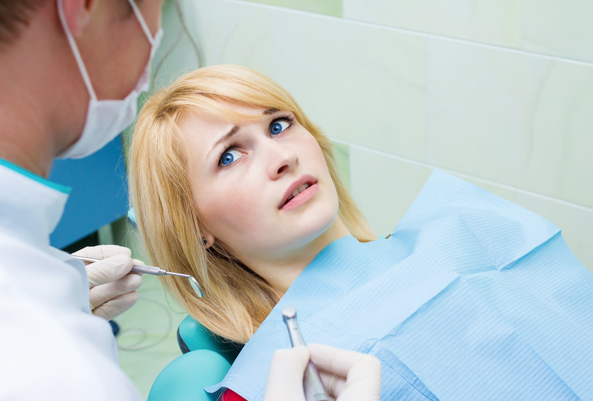 Closeup portrait young terrified girl woman scared at dentist visit, siting in chair looking at doctor doesn't want dental procedure, drilling, tooth extraction, isolated clinic office background