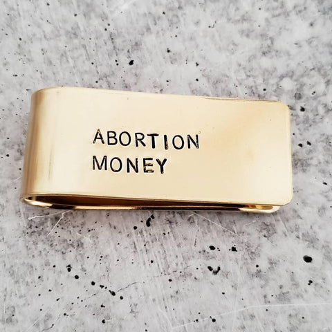 Thick brass money clip hand-stamped with "ABORTION MONEY" in simple uppercase font