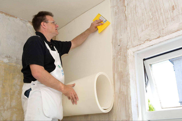 Guy applying wallpaper starting at the top of the wall