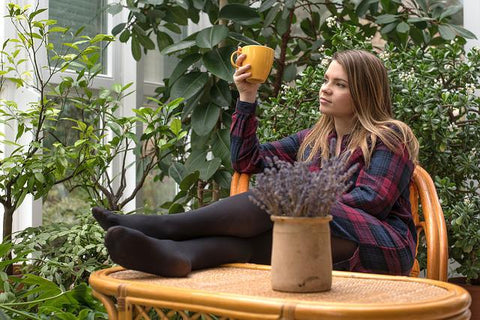 Young female sitting in an outdoor setting dressed warmly and feet on the table enjoying a mug of coffee. Picture from https://www.instagram.com/_.milesz._/ 