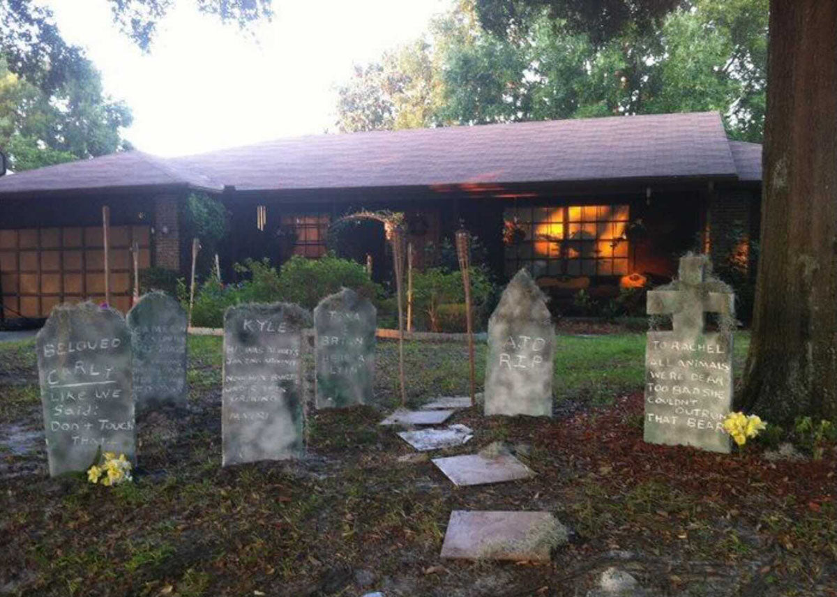Image contains a photo of a house with several fake tombstones in the foreground.