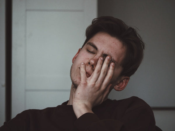 A Man, Sat with Eyes Closed, and Covering the Left Side of His Face with A Hand