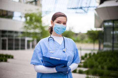 Female doctor holding blue clipboard standing outside hospital or clinic