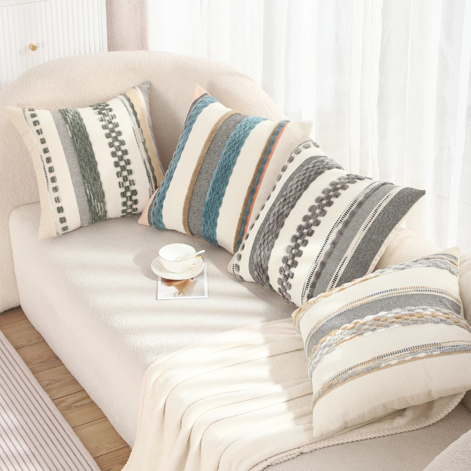 A cozy living room setup featuring a variety of Embroidered Chenille Striped Pillow Throw Covers on a beige couch, accompanied by a white blanket and a teacup on a saucer.