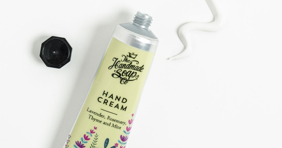Light green hand cream tube with a floral illustration. The tube is open and to the right there is a swirl of hand cream on the surface.