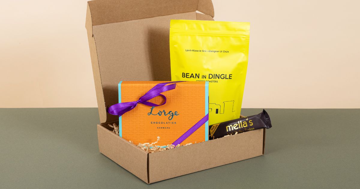 A kraft gift box filled with artisan Irish products including a luxury orange chocolate gift box, a yellow coffee pouch and a brown fudge bar.