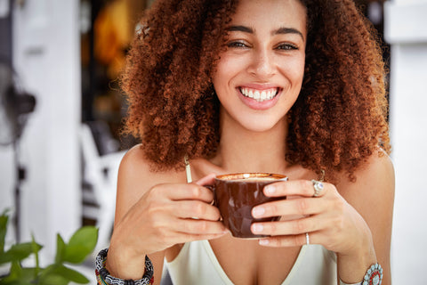 Happy smiley beautiful woman, enjoying a mug of coffee that she is holding with her two hands.