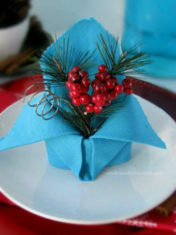 blue linen napkin folded with holiday greenery set on a white plate at a table setting