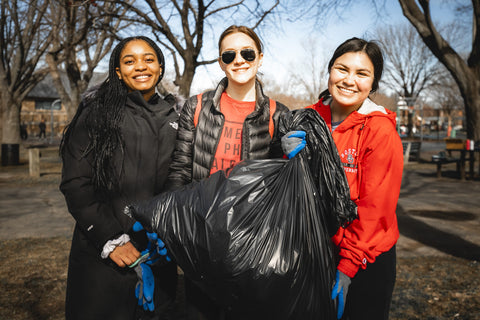 Volunteers at a Boston Harbor Now cleanup. Three women hold a garbage bag full of litter they picked up during the cleanup event and smile at the camera.
