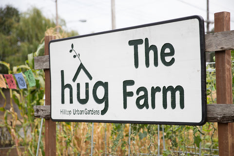 A sign for Hilltop Urban Gardens that reads "hug, The Farm" in an outdoor garden