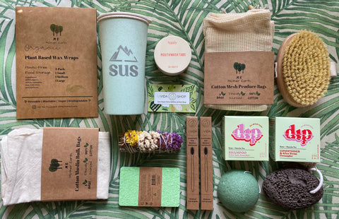 Zero waste products for Uvida Shop. Photo includes wax wraps, reusable coffee cup, mouthwash tablets, dry body brush, cotton produce and bulk bags, plastic-free sponges, sage stick, bamboo toothbrushes, shampoo and conditioner bars, facial sponge, and lava pumice stone.