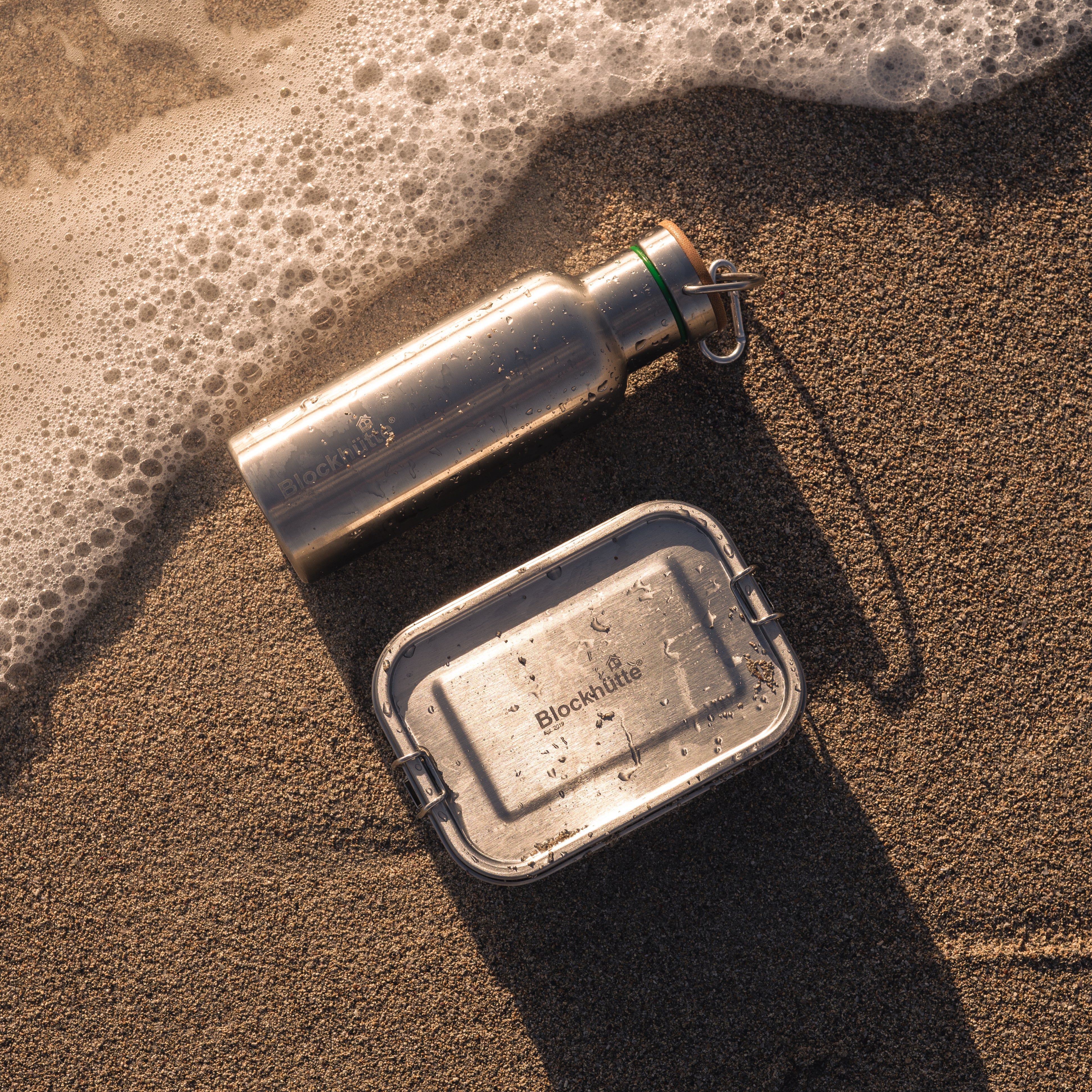 Blockhuette stainles steel lunch box and water bottle lying at the beach