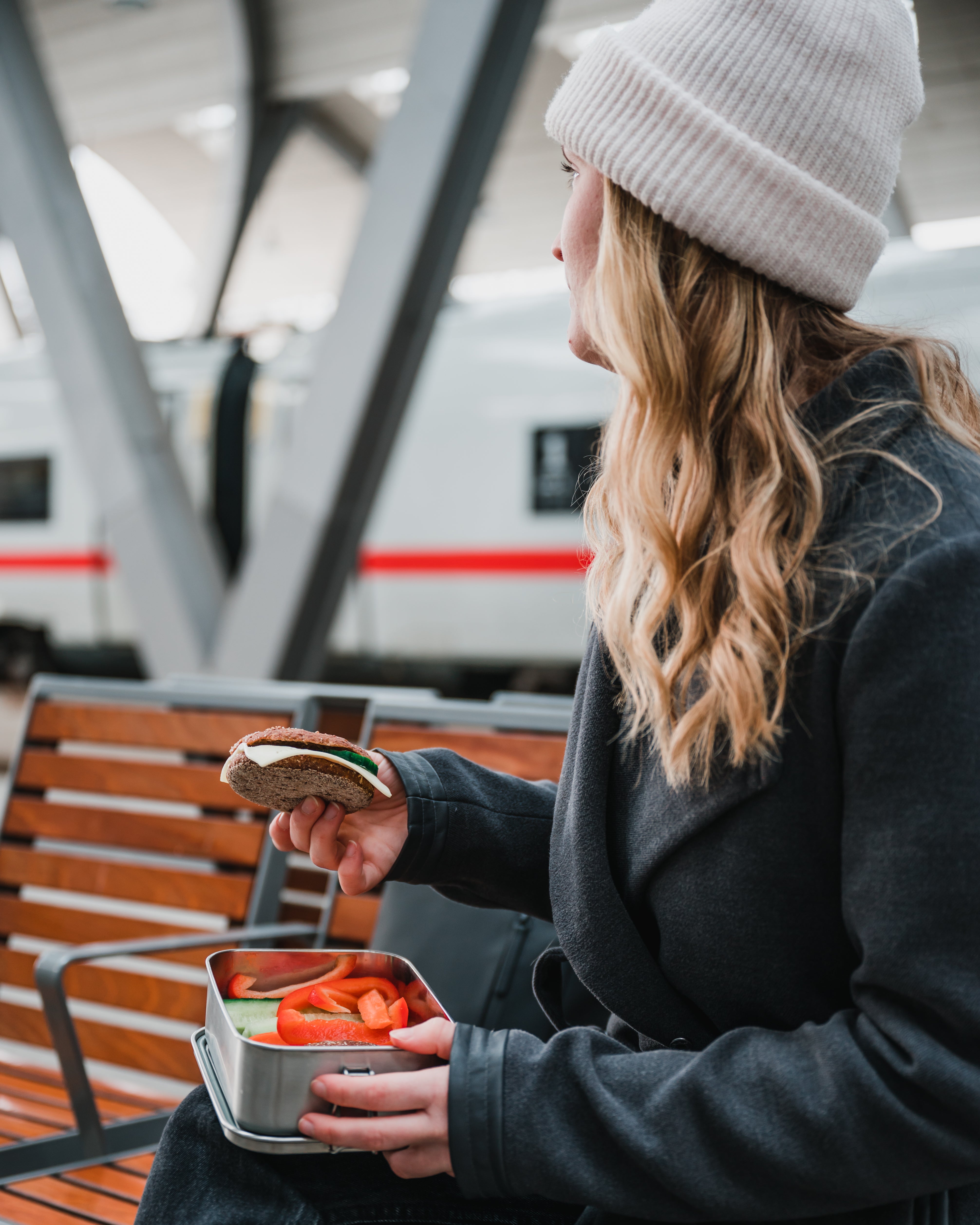 A girl eating a sandwich out of the Blockhuette stainless steel lunch box at a train station