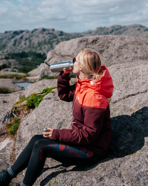 Frau sitzt auf einem Felsen und trinkt aus der Blockhütte Edelstahl Trinkflasche