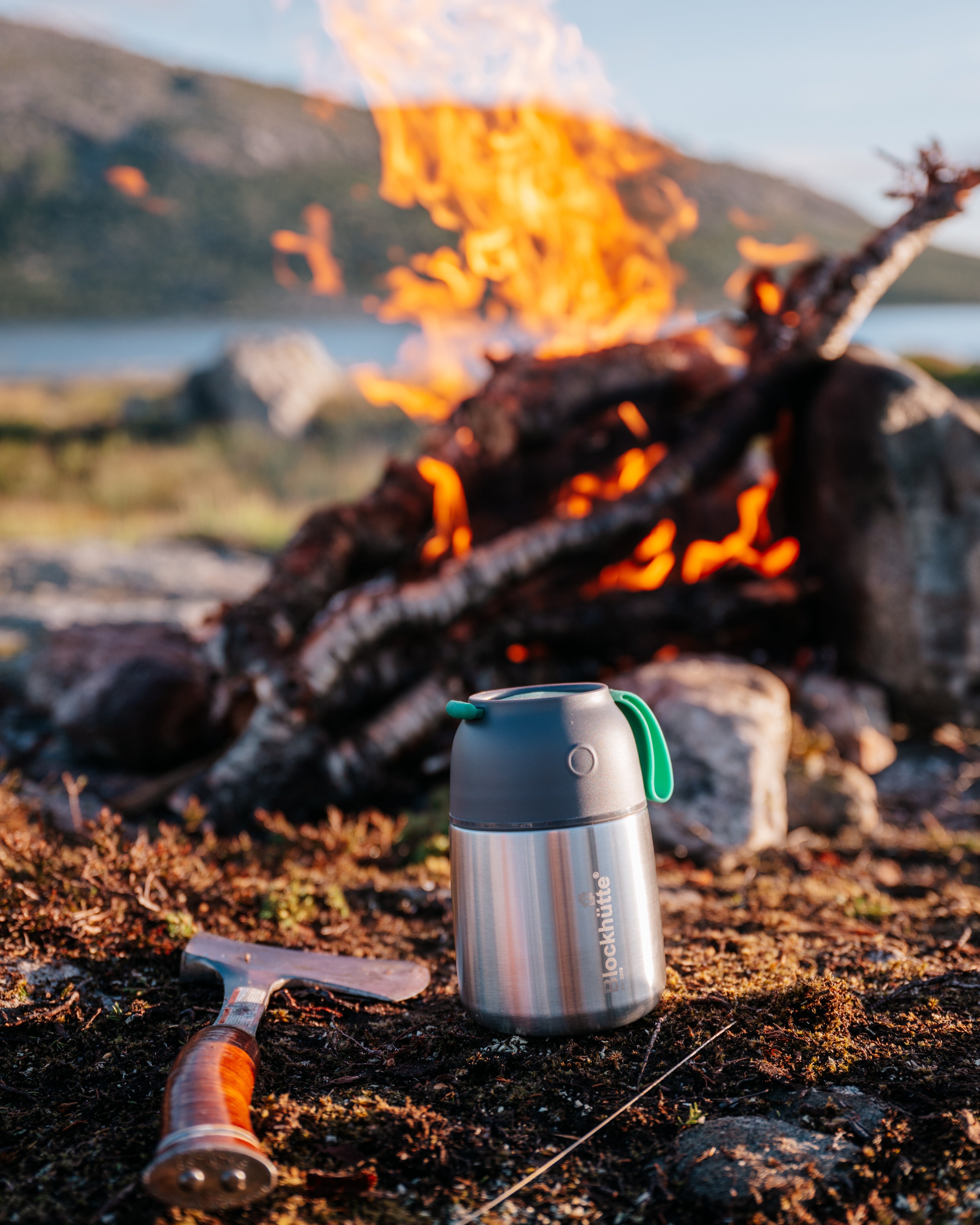 Blockhuette stianless steel insulated food jar in front of a bonfire, right next to an axe