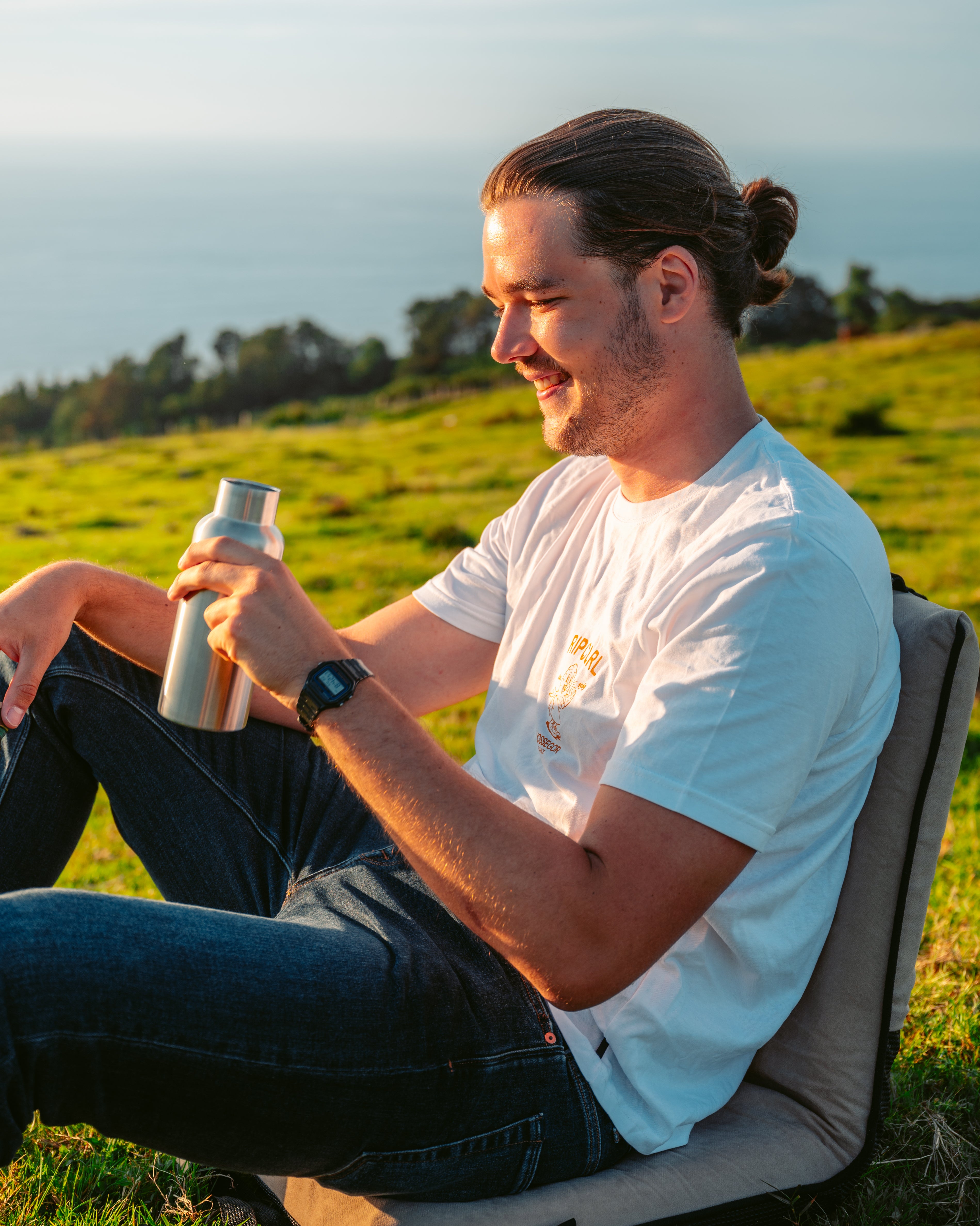 A guy holding Blockhuette stainless steel water bottle sitting on a chair on a field