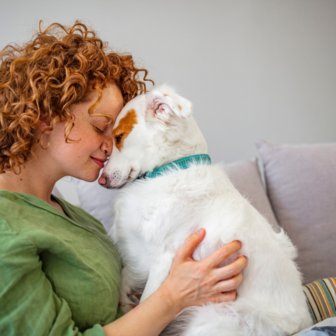 photo of a woman nuzzling her small white dog on the couch