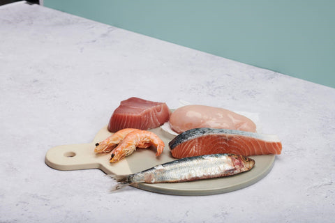 Fresh chicken breast, fish, and shrimp placed on a charcuterie board on a marble-finish counter