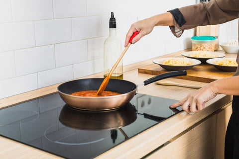 A person mixing homemade gravy for cats in a pan with a wooden spatula on an induction stove