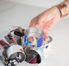 An array of Giftolgie cuffs with a model showing the message inscirbed inside: Live life in full bloom.