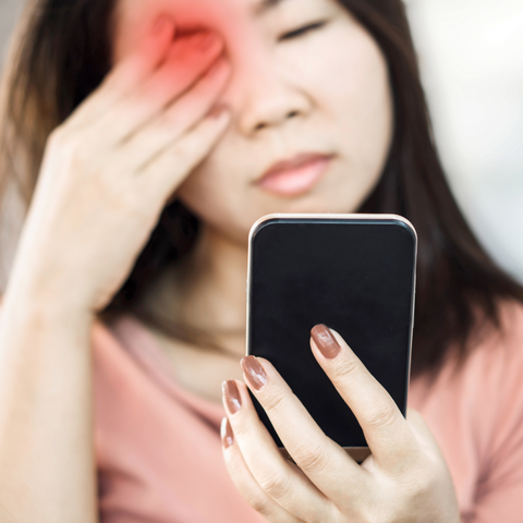 Girl holding sore eye whilst looking at ipad