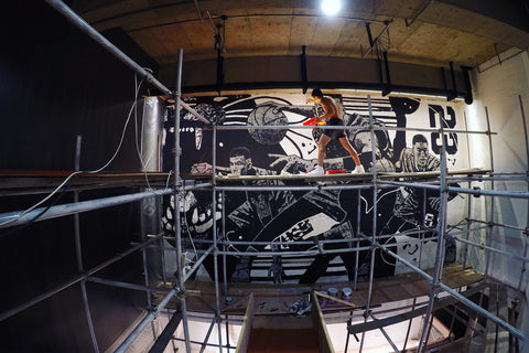 Gian painting a black and white mural while standing on scaffolding