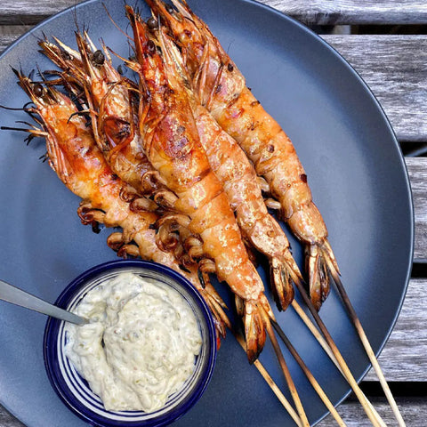 Skewered grilled truffled prawns on a plate with tartar sauce